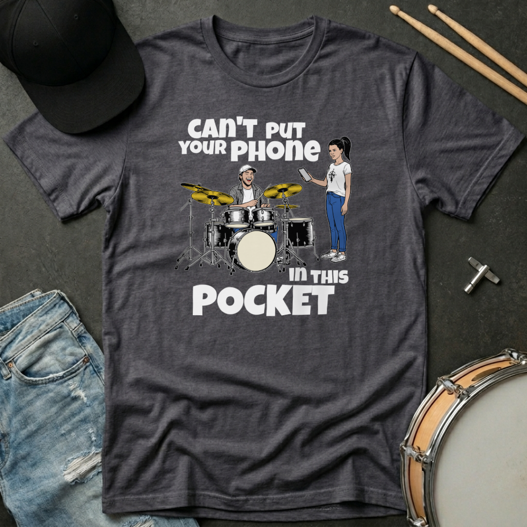 Gray t-shirt with graphic design of a drummer and person with text 'Can't put your phone in this pocket' on a dark surface with drumsticks and jeans.