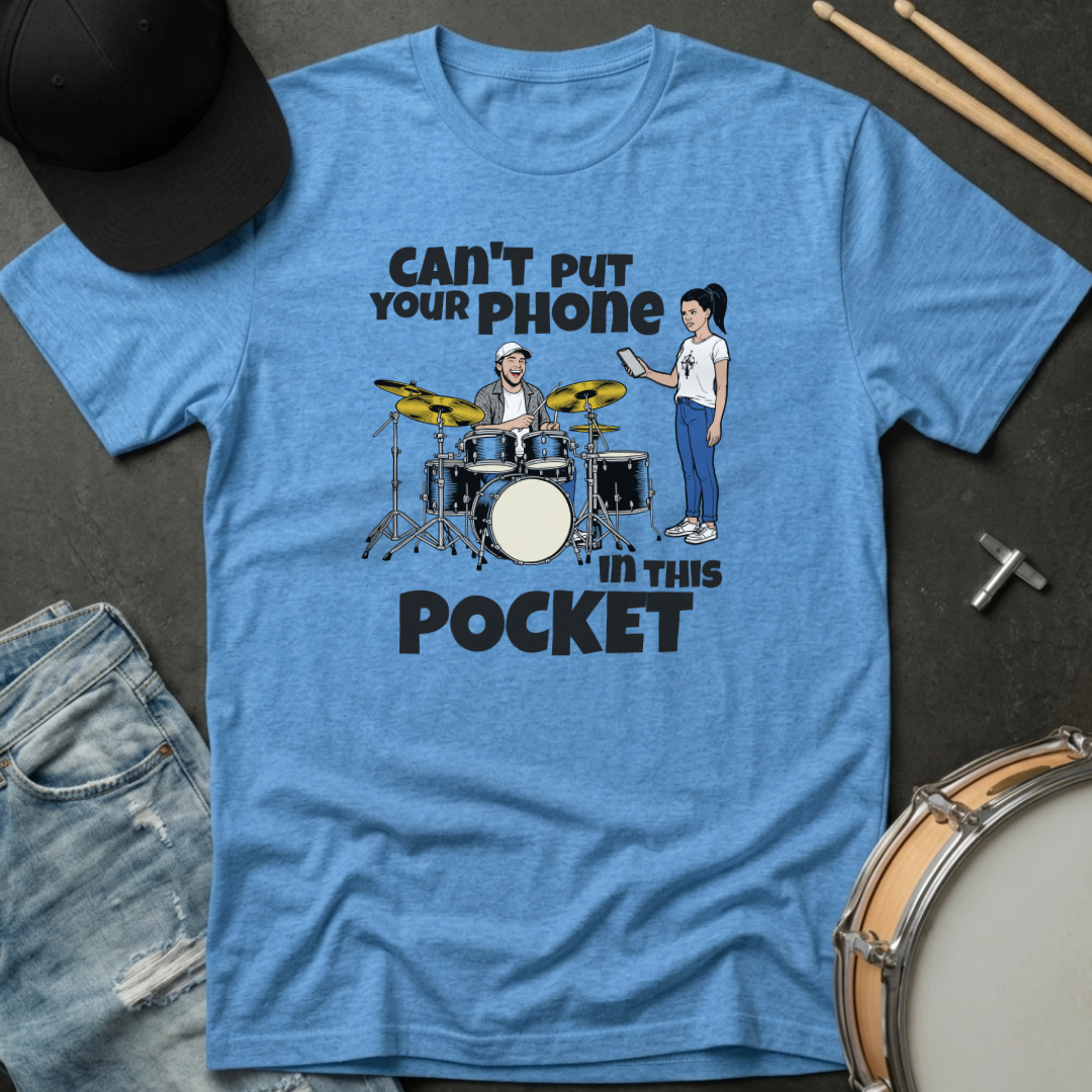 Blue t-shirt with graphic design of a drummer and text 'Can't put your phone in this pocket' on a dark surface with drumsticks and jeans.