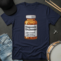 Navy blue t-shirt with a bottle graphic and text 'Diagnosis: Drummer' on a dark surface with drumsticks and a cap.