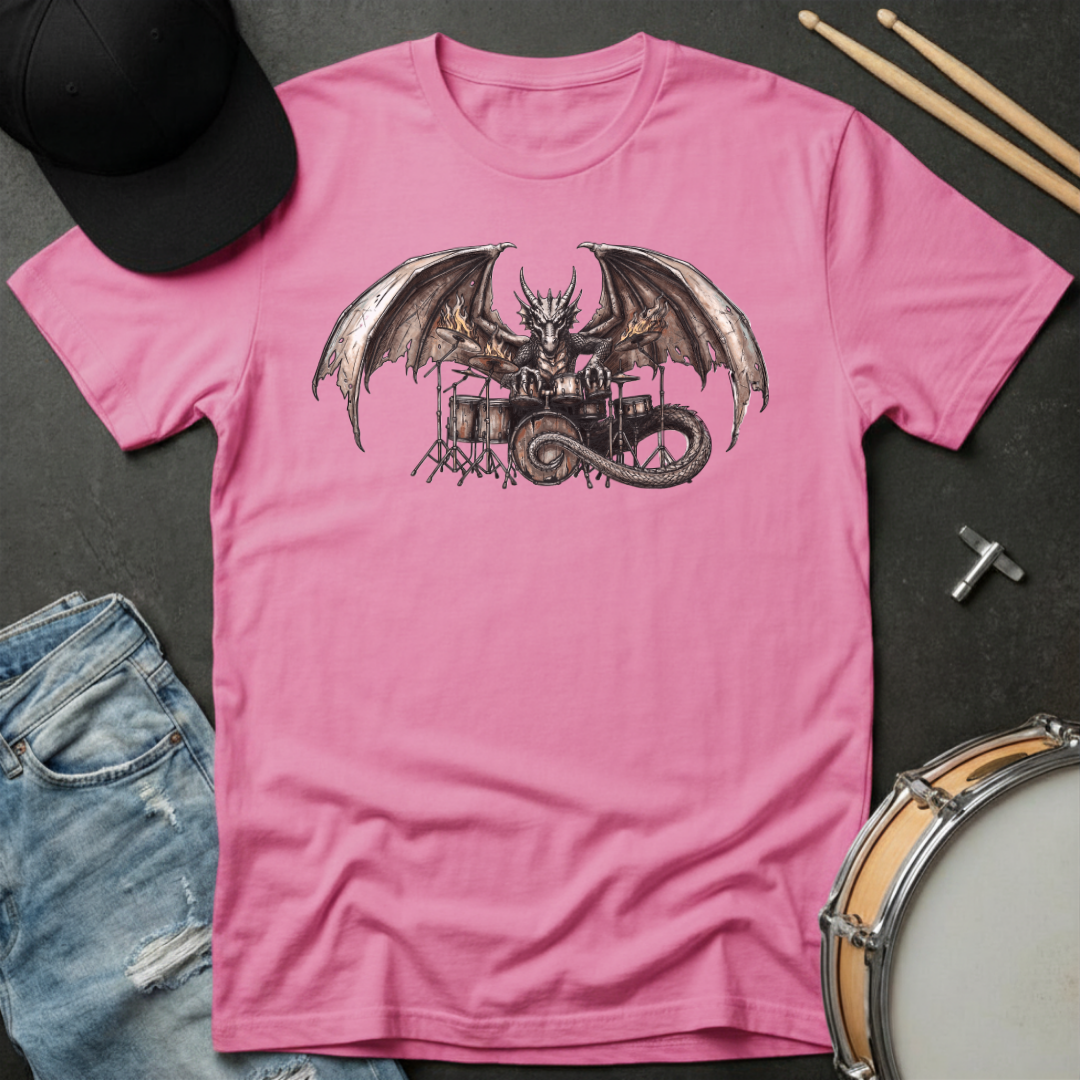 Pink t-shirt with dragon playing drums graphic on a dark surface with casual items.