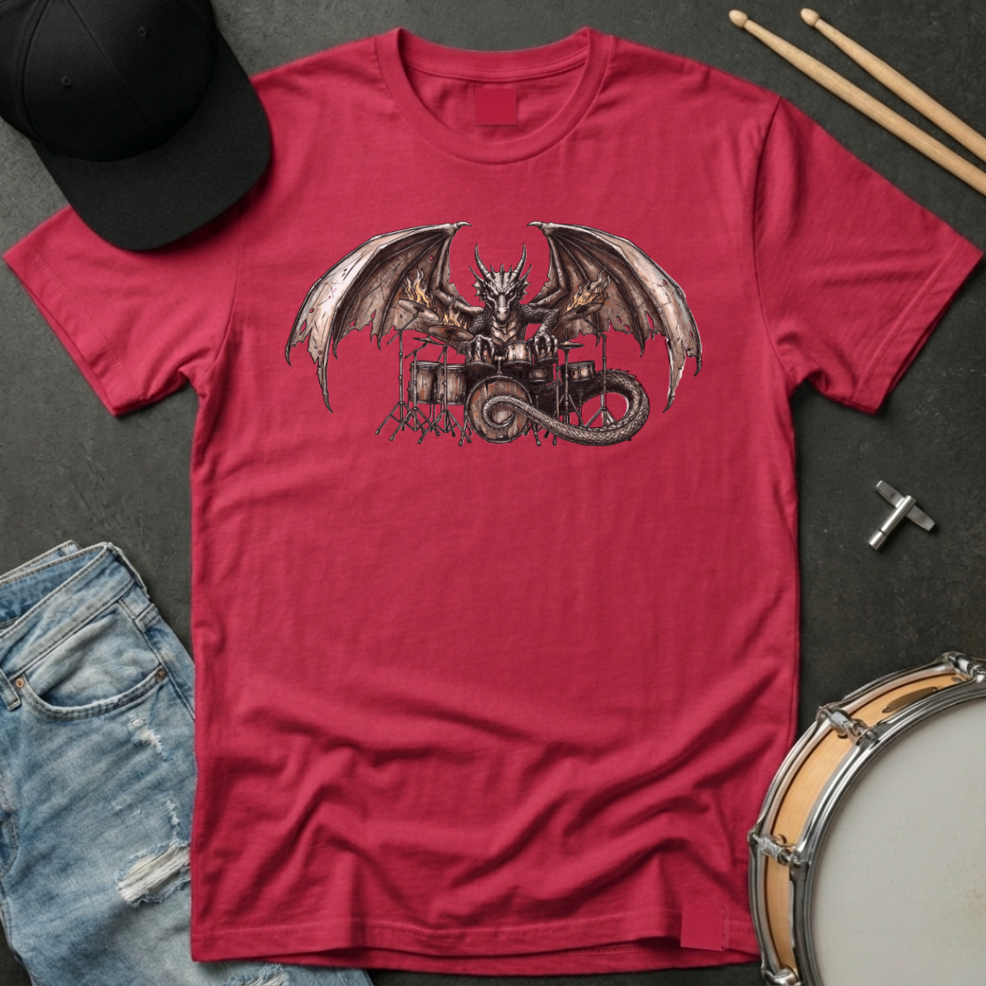 Red t-shirt with a dragon playing drums graphic on a dark surface with a cap, jeans, and drumsticks.