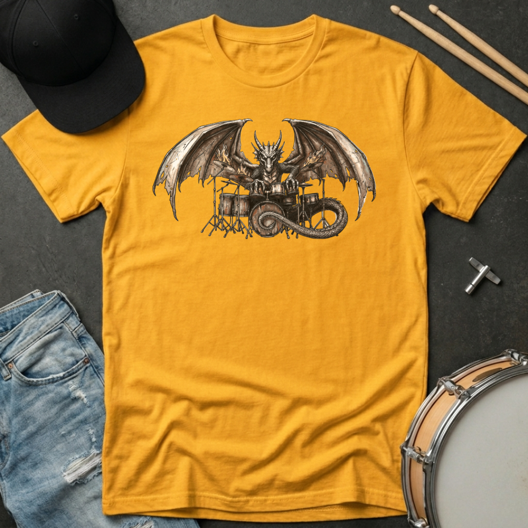 Yellow t-shirt with a dragon playing drums graphic on a dark surface with casual items.