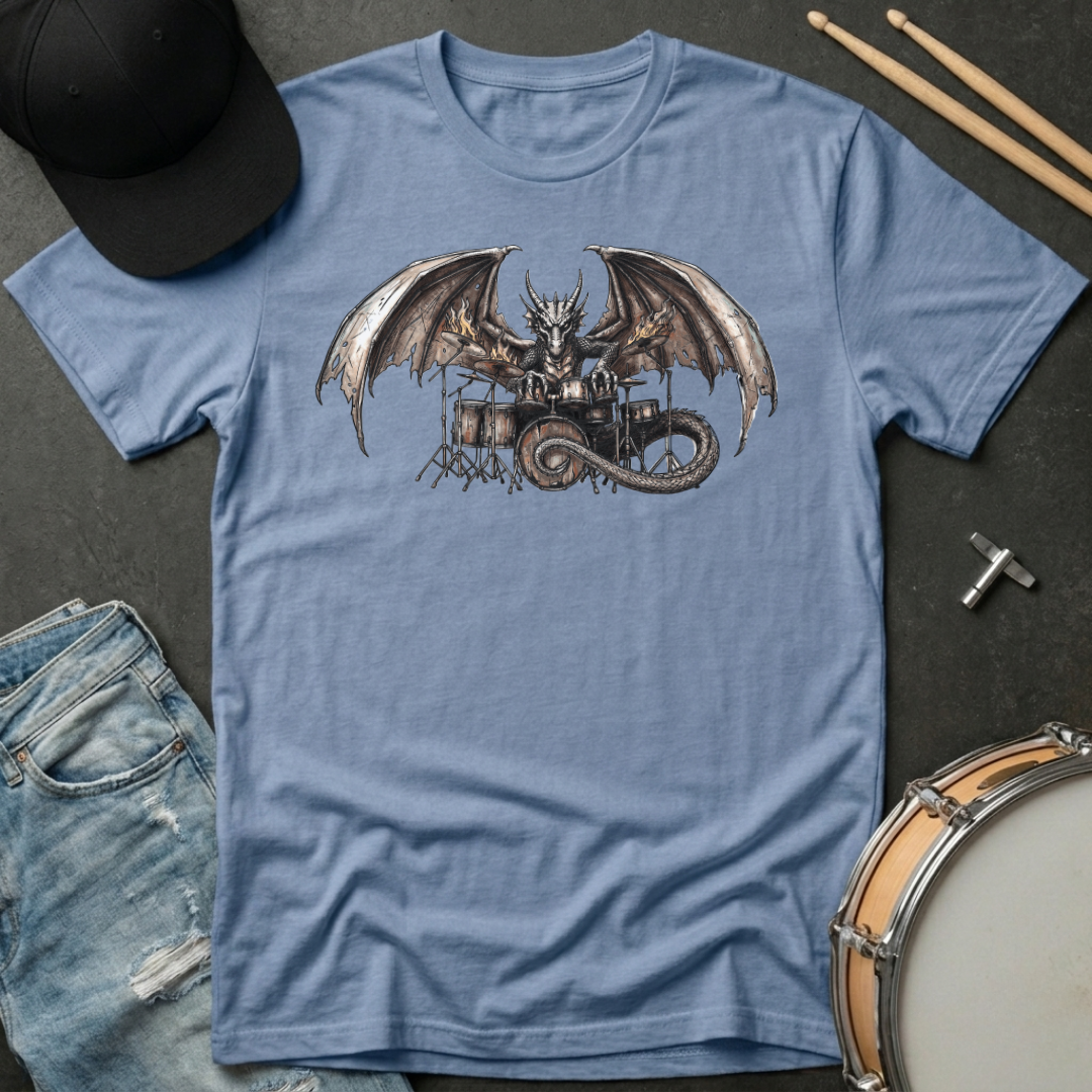 Blue t-shirt with a dragon playing drums graphic on a dark surface with casual items.
