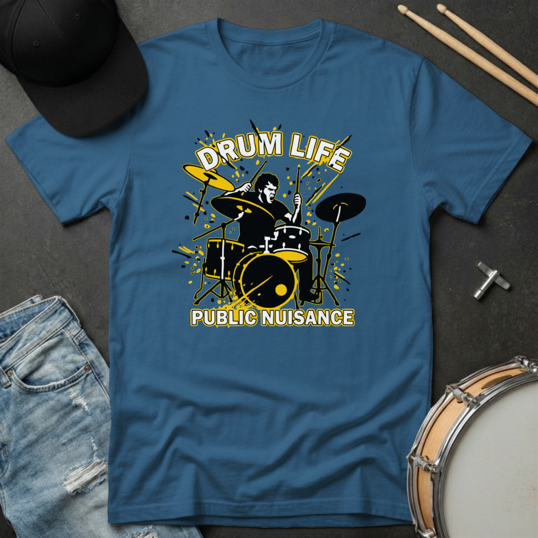 Blue t-shirt with 'Drum Life Public Nuisance' graphic on a dark surface with drumsticks and a hat.