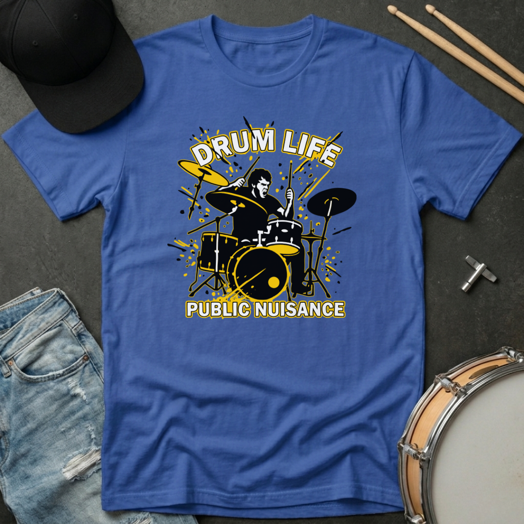Blue t-shirt with drum design and text 'Drum Life Public Nuisance' on a dark surface with drumsticks and cap.