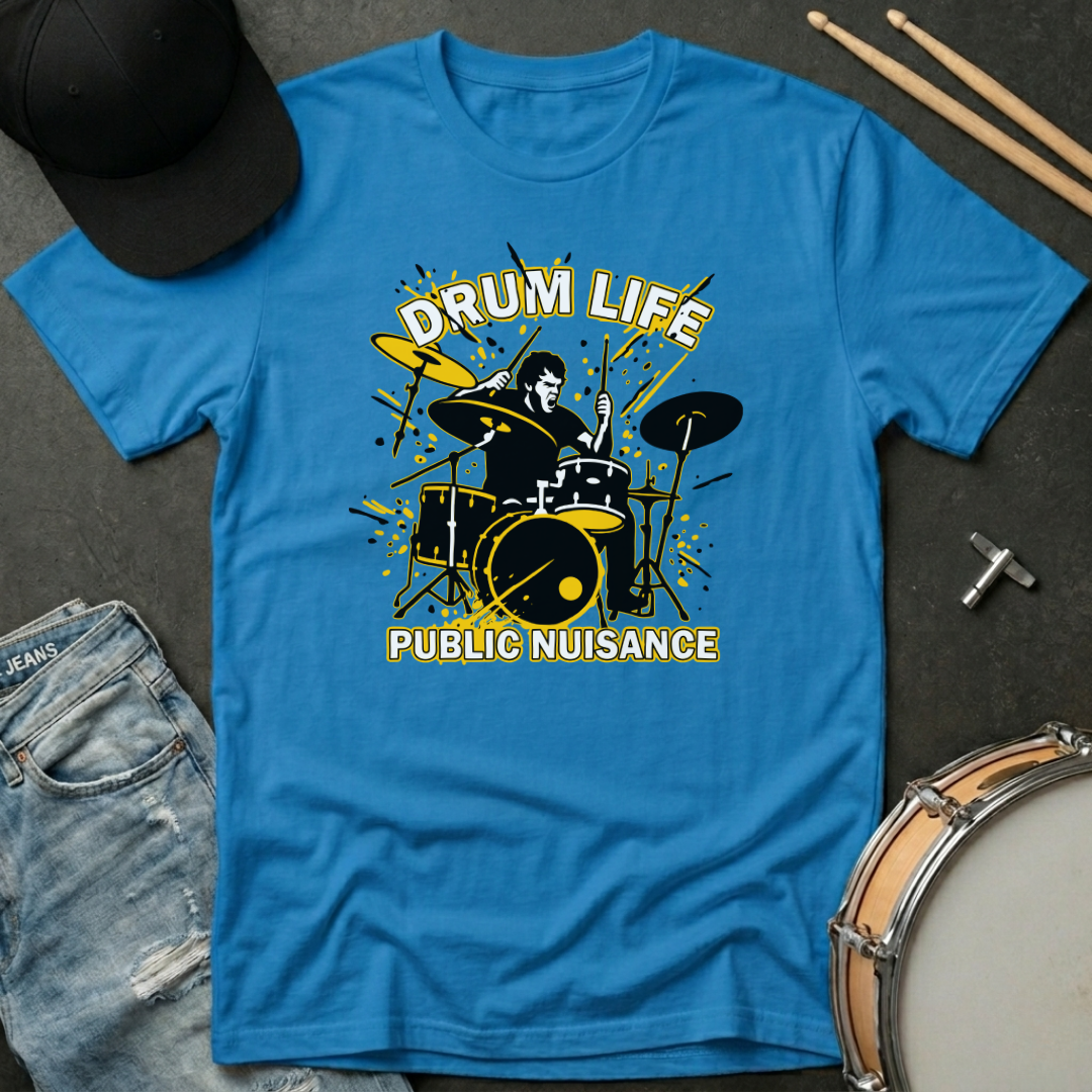 Blue t-shirt with drum design and text 'Drum Life Public Nuisance' on a dark surface with drumsticks and a cap.