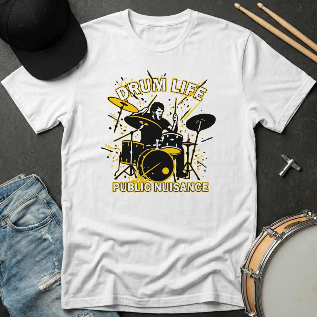 White t-shirt with drum design and text 'Drum Life Public Nuisance' on a dark surface with drumsticks and cap.