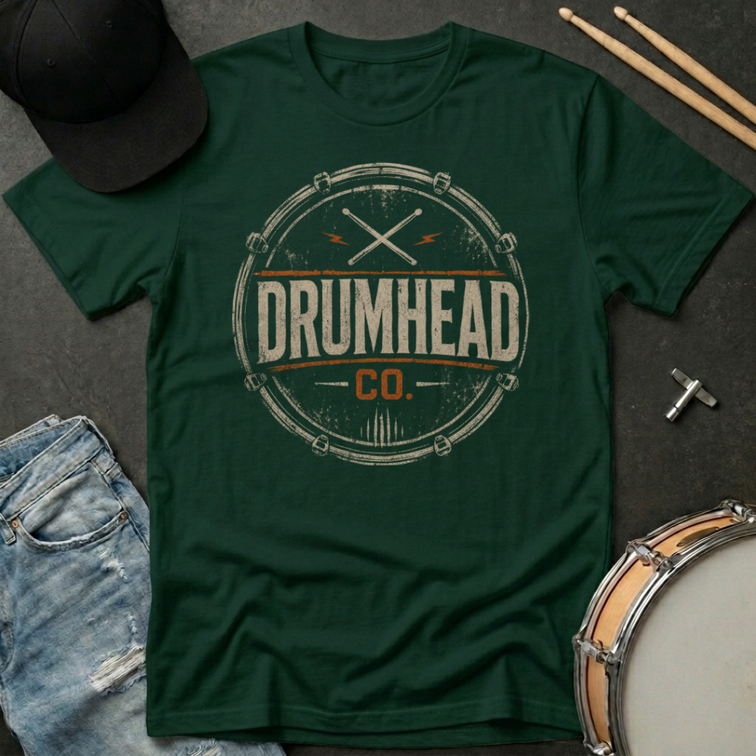 Green t-shirt with 'DRUMHEAD CO.' design on a dark surface with drumsticks and a cap.
