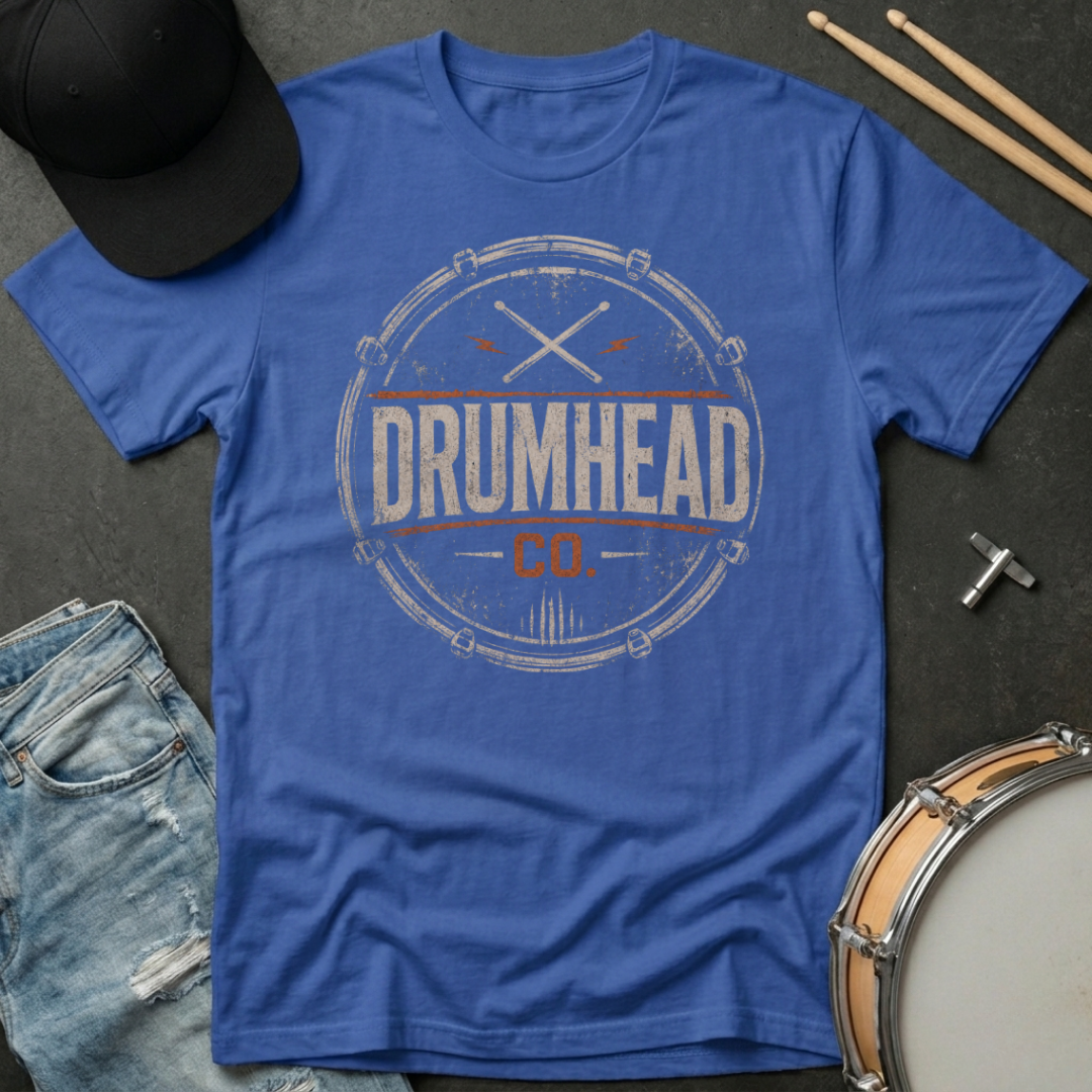 Blue t-shirt with 'DRUMHEAD CO.' design on a dark surface with drum components.