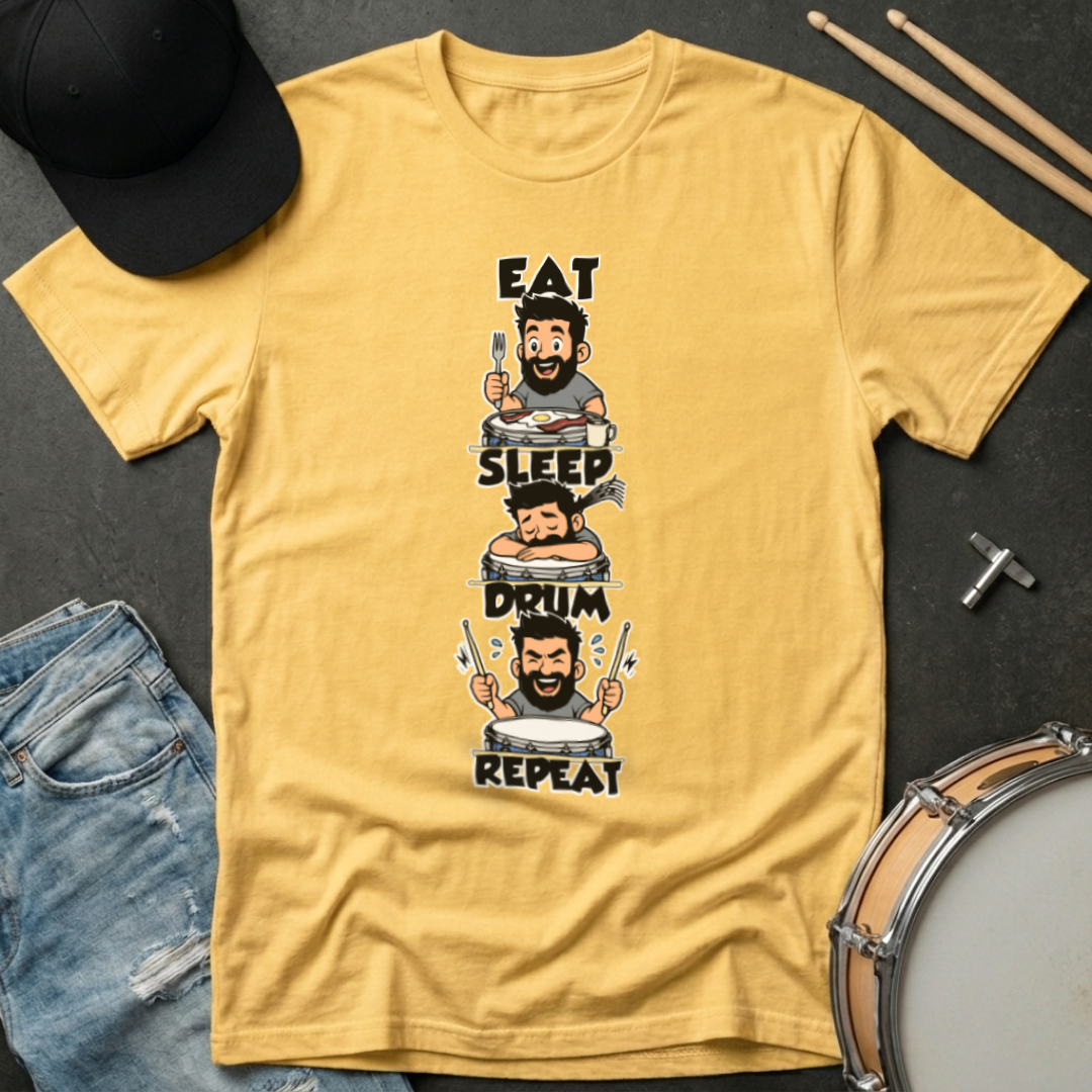 Yellow t-shirt with drum-themed graphic and text on a dark surface with drumsticks and jeans.