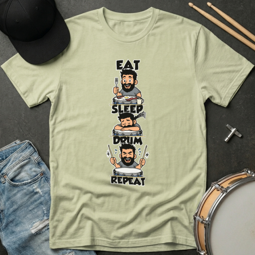 Light green t-shirt with a graphic design featuring a drummer, placed on a dark surface with drumsticks and a hat.