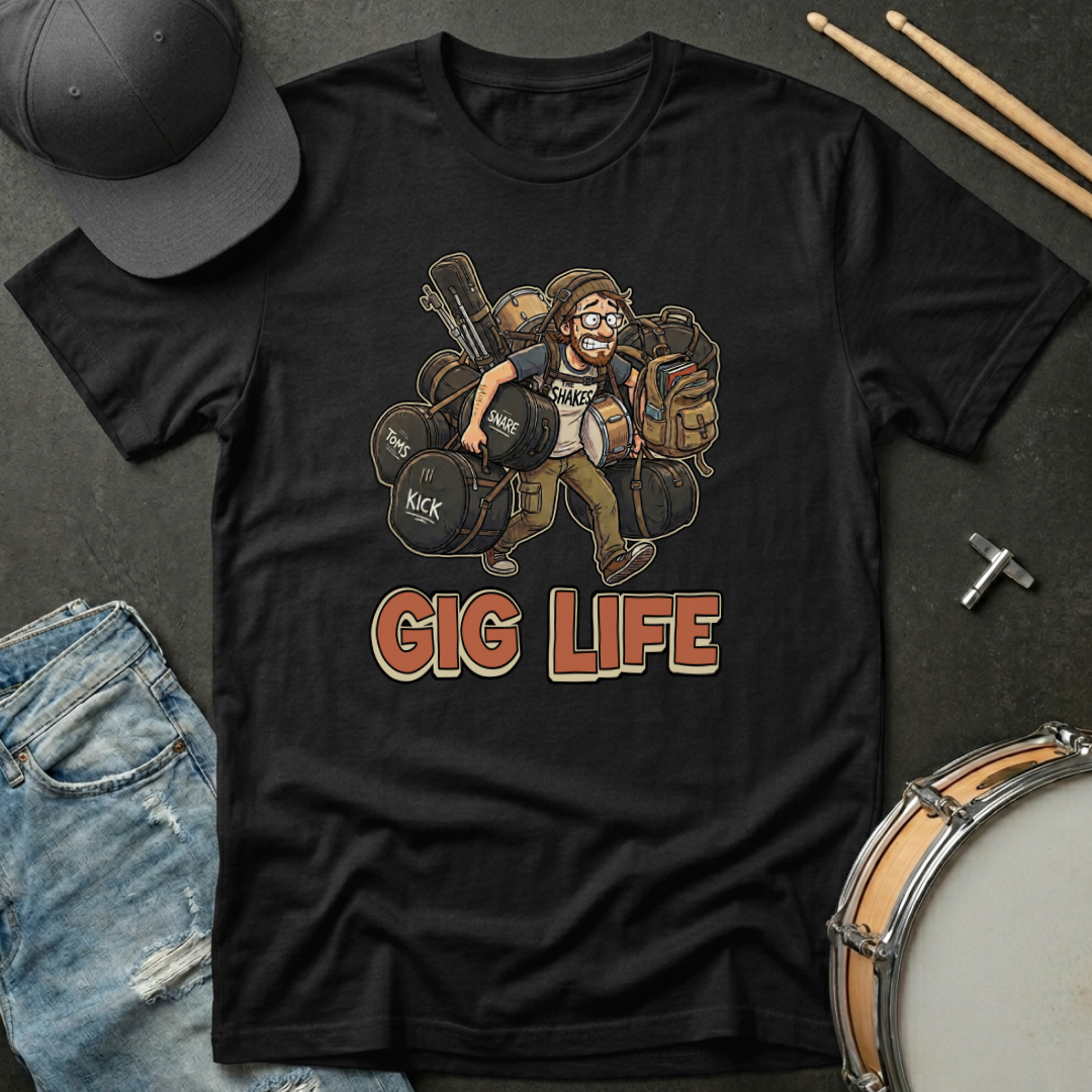 Black t-shirt with 'Gig Life' graphic featuring a musician and musical instruments, placed on a dark surface with a cap, jeans, and drumsticks.
