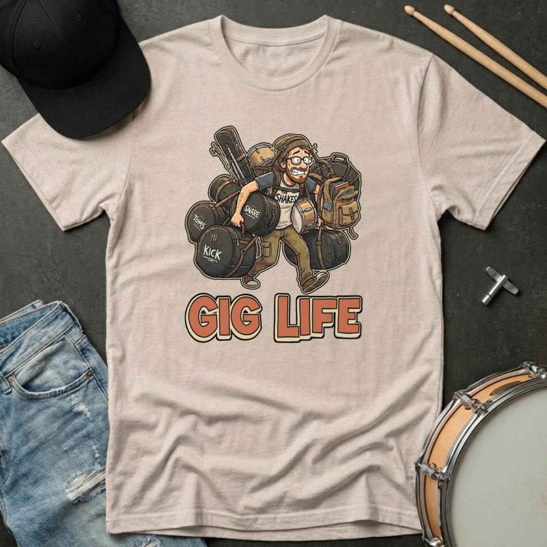 Beige t-shirt with 'Gig Life' graphic featuring a drummer, surrounded by drumsticks, jeans, and a hat on a dark surface.