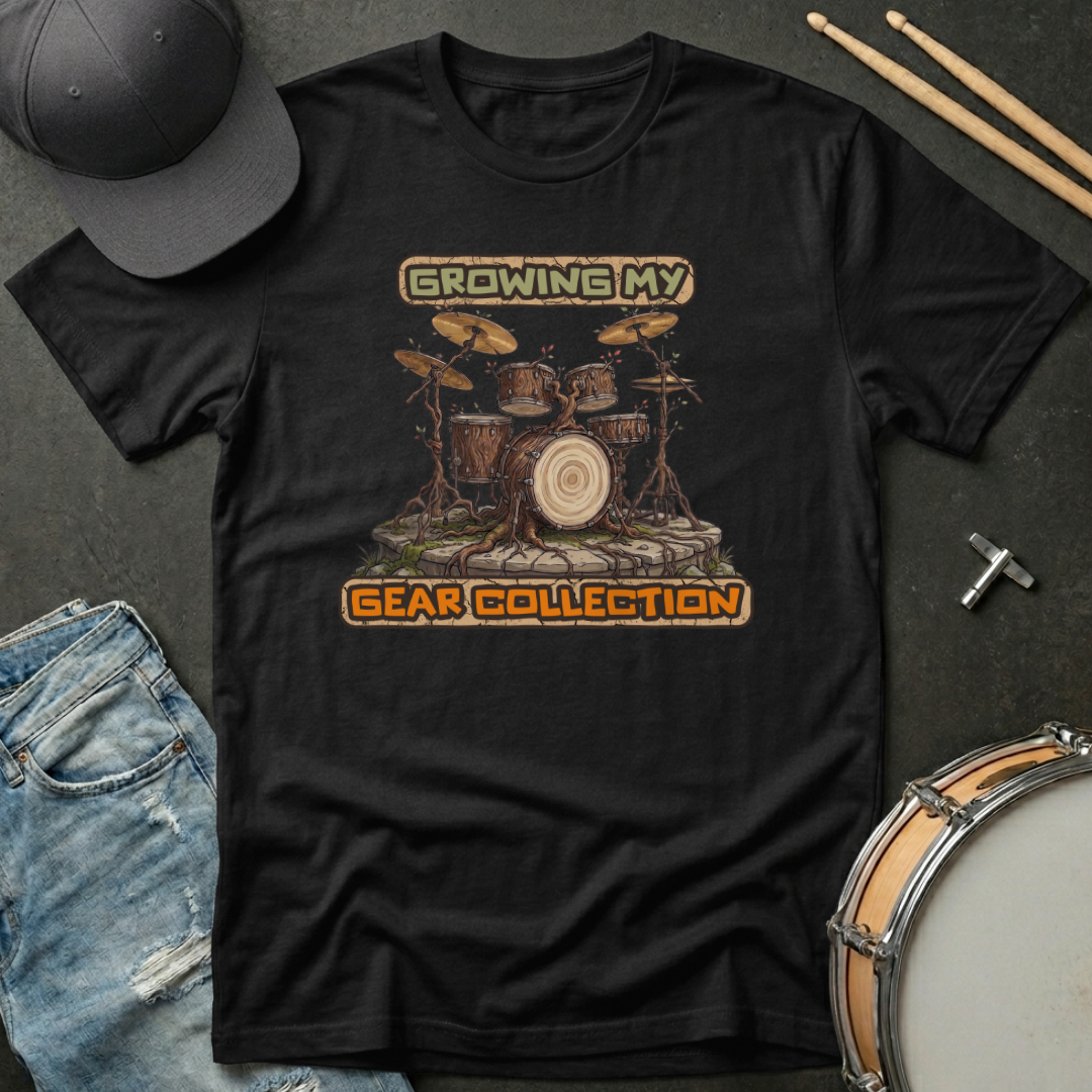 Black t-shirt with drum set graphic and text 'Growing My Gear Collection' on a dark surface with drumsticks and a cap.
