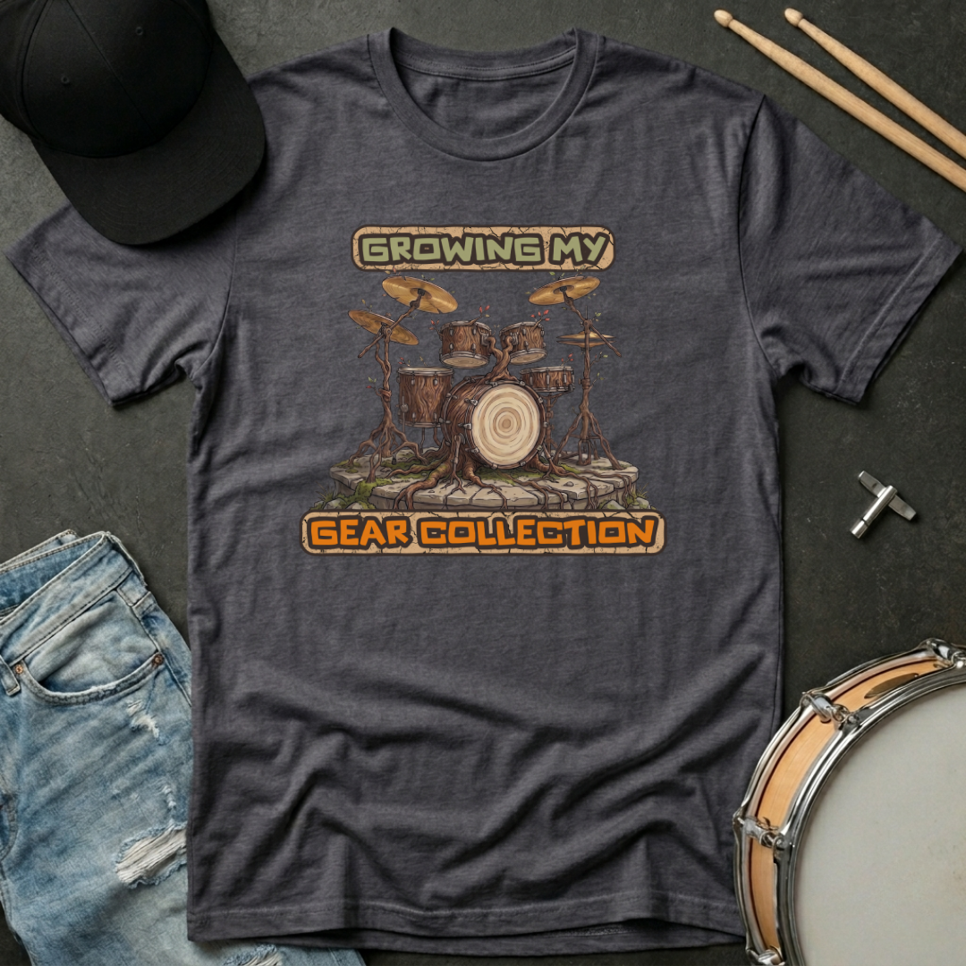 Gray t-shirt with a drum set graphic and text on a dark surface with casual items.
