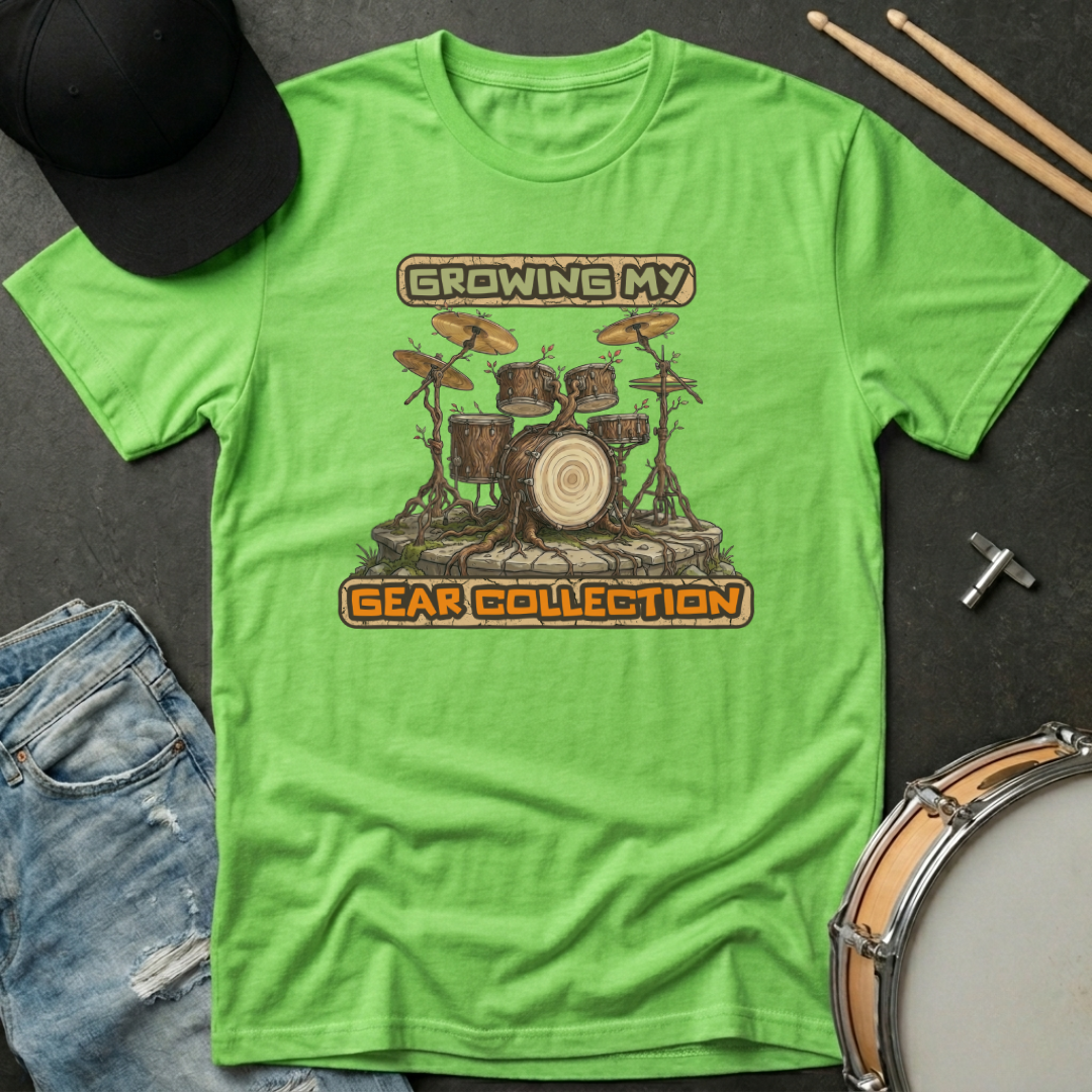 Green t-shirt with drum set graphic and text 'Growing My Gear Collection' on a dark surface with drumsticks and jeans.