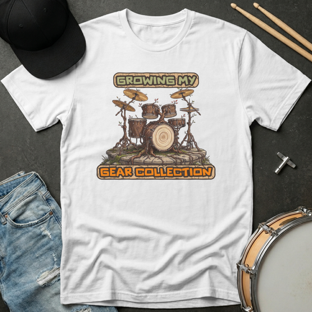 White t-shirt with drum set graphic and text 'Growing My Gear Collection' on a dark surface with drumsticks and jeans.