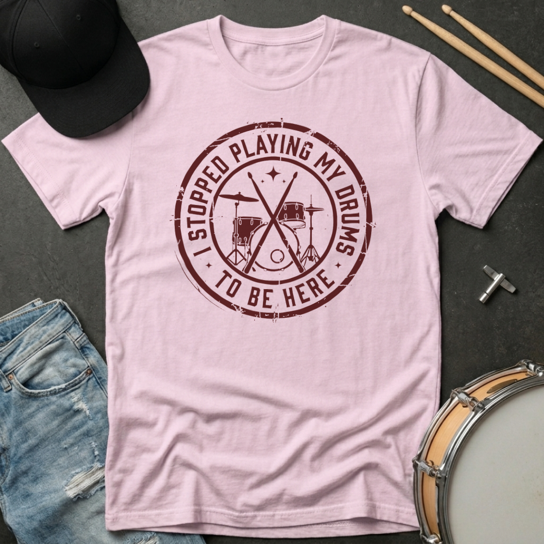 Pink t-shirt with a graphic and text on a dark surface with casual items.