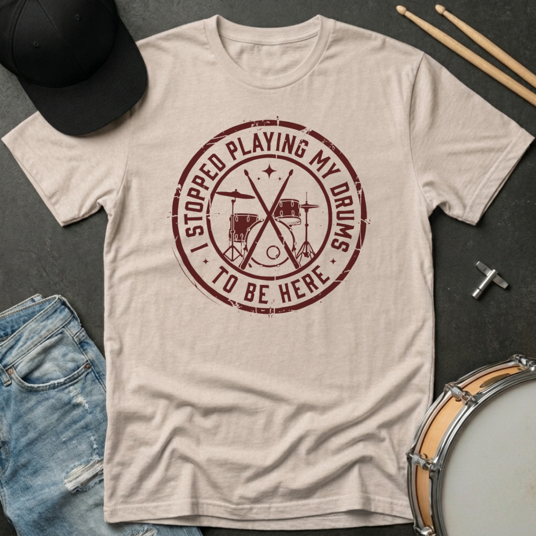 Beige t-shirt with red graphic and text on a dark surface with casual items.