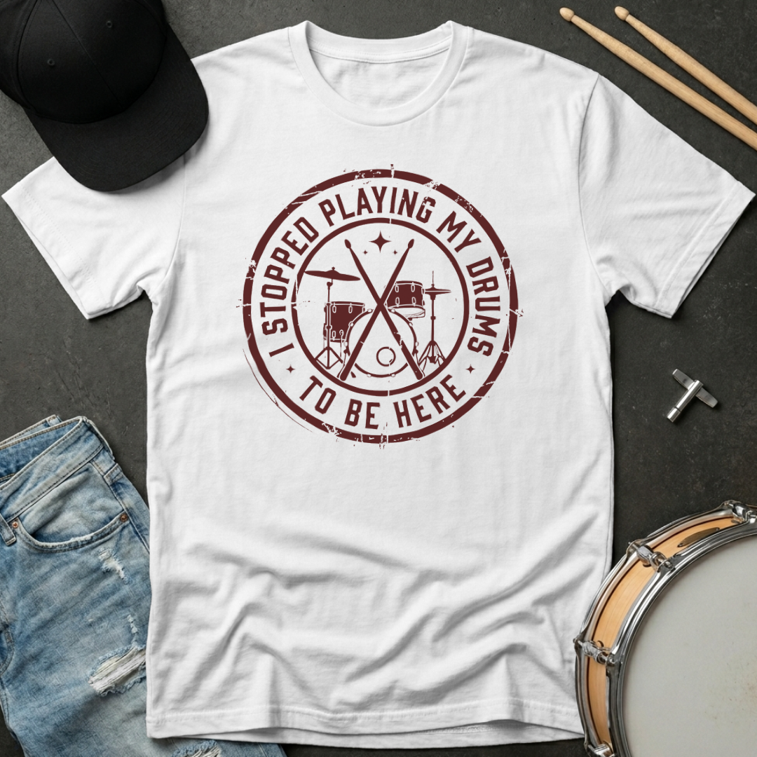 White t-shirt with red graphic and text on a dark surface with casual items.