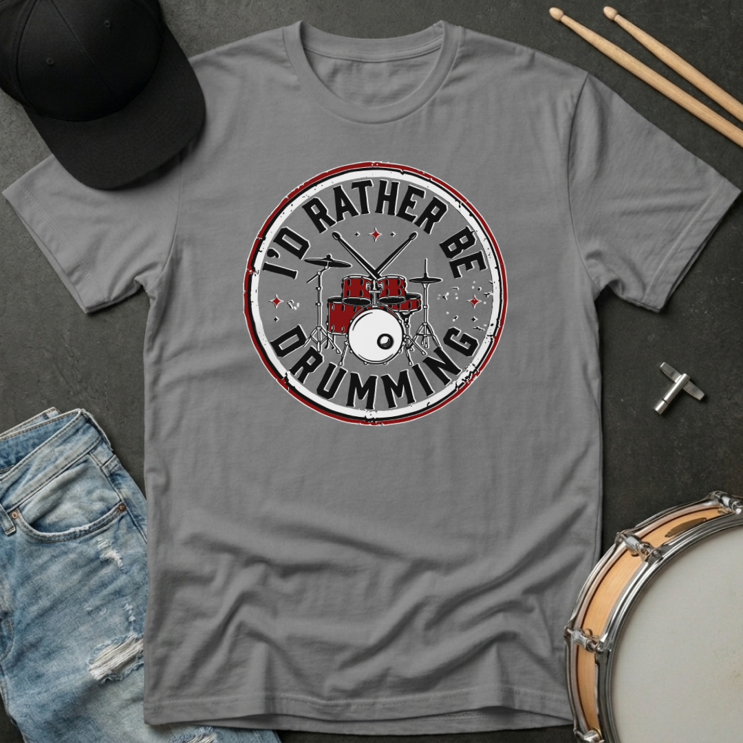 Gray t-shirt with 'I'd Rather Be Drumming' design on a dark surface with drumsticks and a hat.