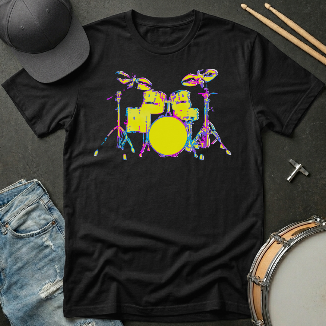 Black t-shirt with colorful drum set graphic on a dark surface with casual items.