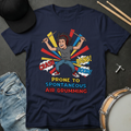 Navy blue t-shirt with a graphic of a person air drumming, surrounded by colorful text and symbols on a dark surface with casual items.