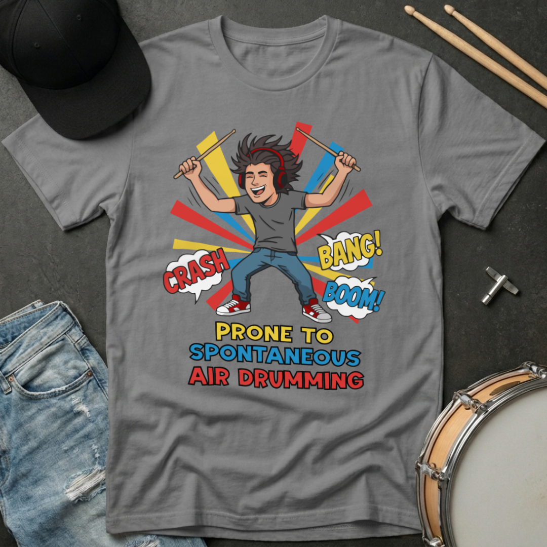 Gray t-shirt with a graphic of a person air drumming and text, surrounded by casual items like jeans and a hat.