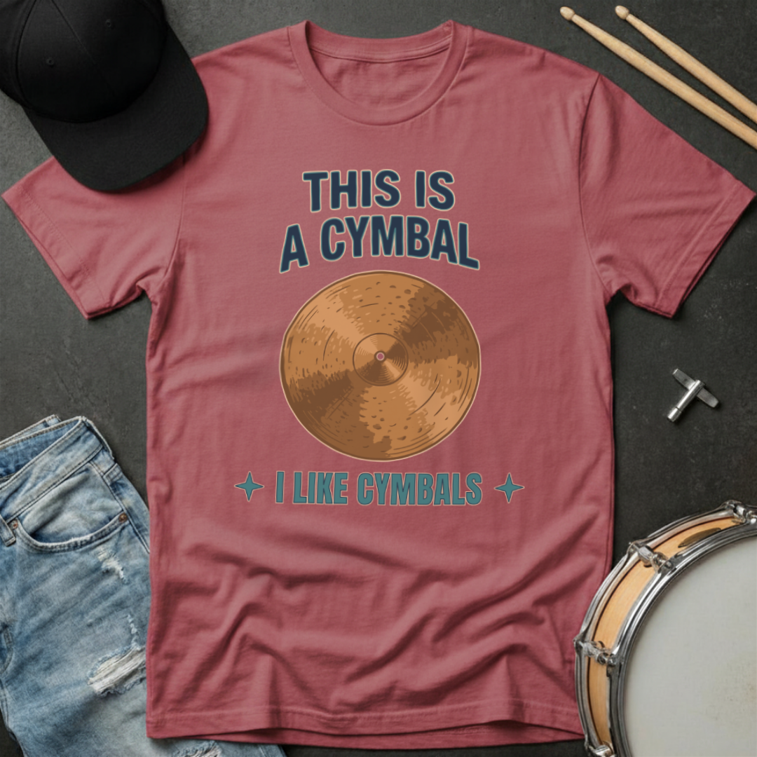 Maroon t-shirt with cymbal graphic and text on a dark surface with drumsticks and jeans.