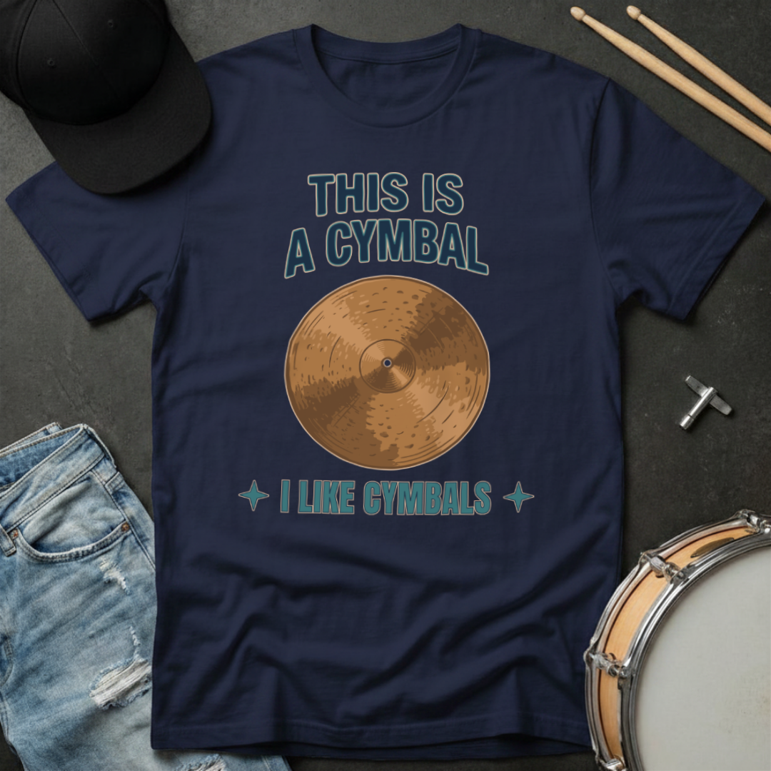 Navy blue t-shirt with cymbal graphic and text on a dark surface with drumsticks and cap.