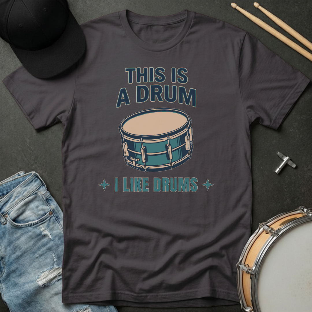 Dark gray t-shirt with drum graphic and text on a dark surface with drumsticks and a hat.