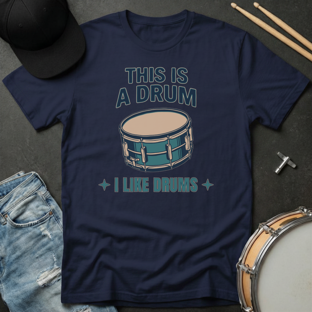 Navy blue t-shirt with drum graphic and text on a dark surface with drumsticks and a cap.