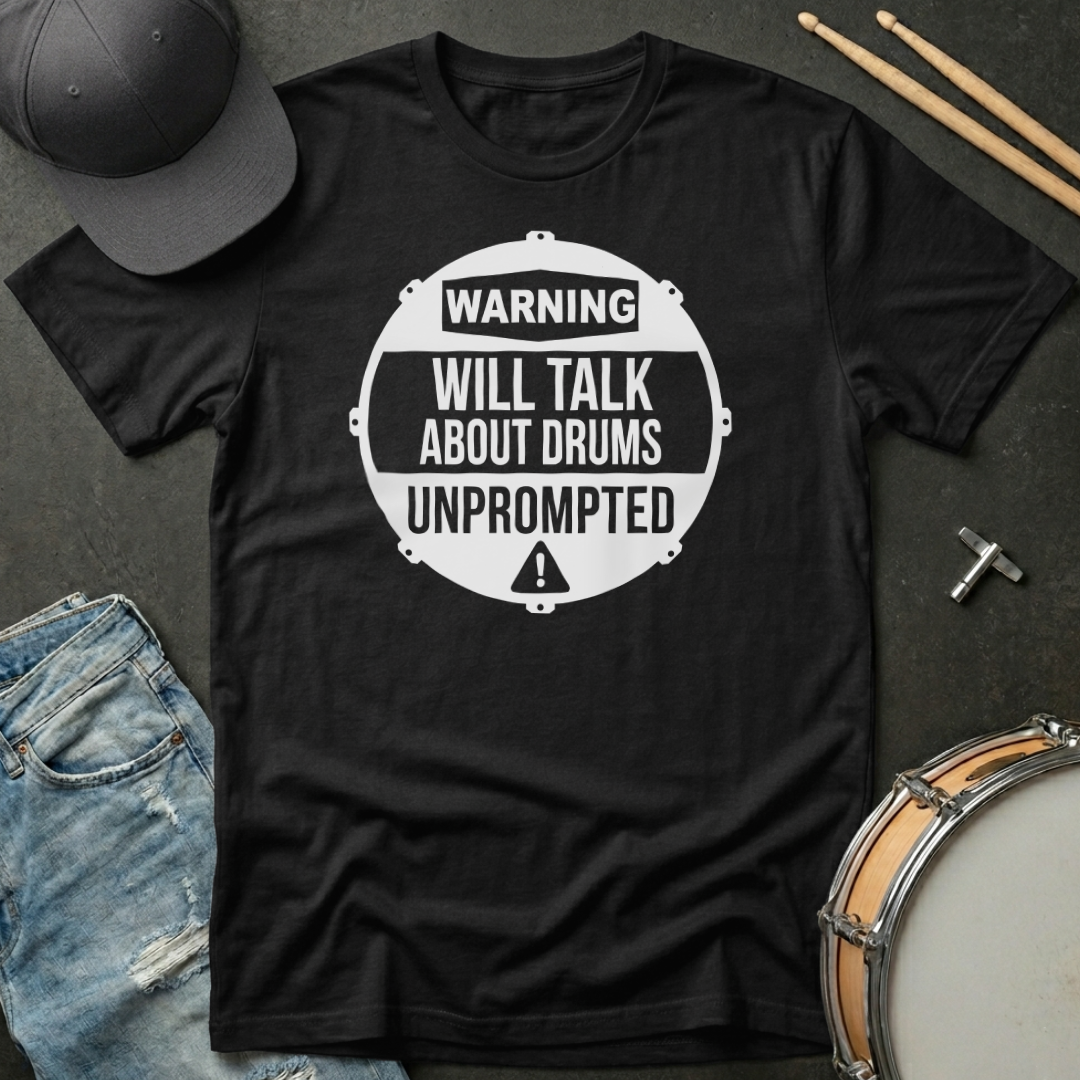 Black t-shirt with 'Warning: Will Talk About Drums Unprompted' text on a dark surface with drumsticks and a hat.