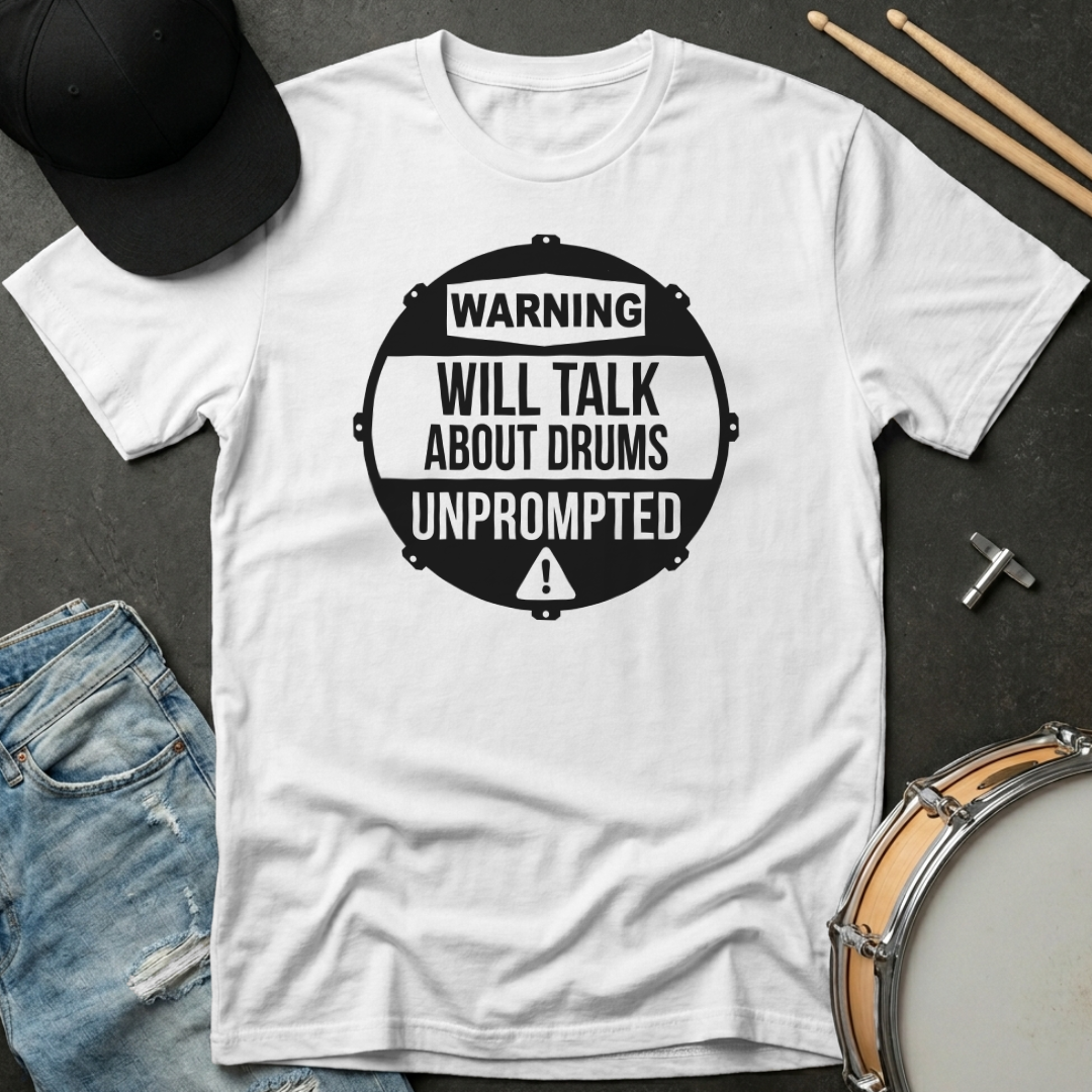 White t-shirt with 'Warning: Will Talk About Drums Unprompted' design on a dark surface with drumsticks and a cap.