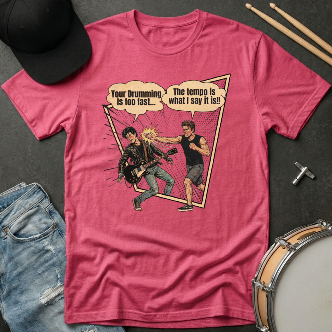Pink t-shirt with graphic design of two drummers and text, placed on a dark surface with a hat, jeans, and drumsticks.