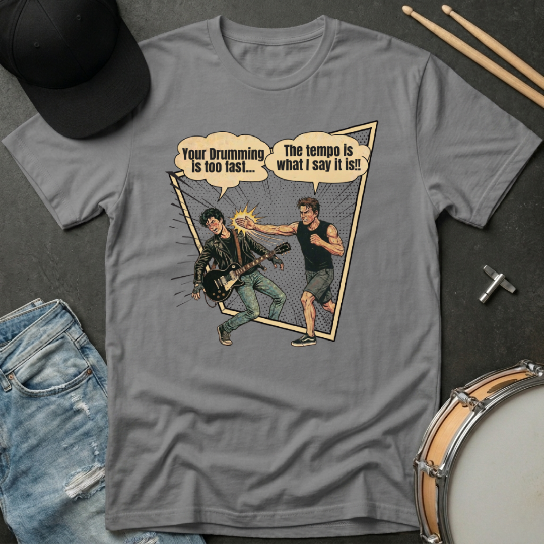 Gray t-shirt with graphic design of two musicians and text, placed on a dark surface with drumsticks and jeans.